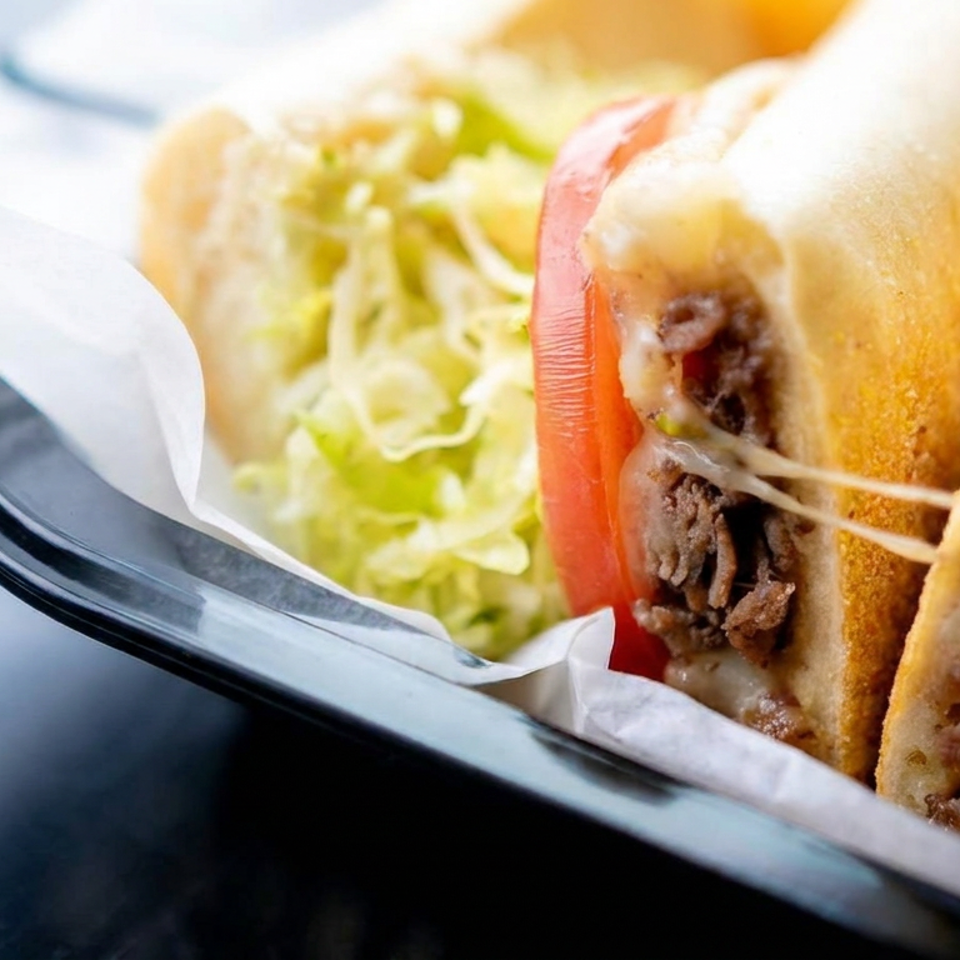Two toasted pita sandwiches filled with sliced beef, melted cheese, lettuce, and tomato on a black plate.